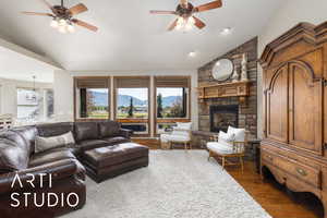 Living area featuring vaulted ceiling, ceiling fan, plenty of natural light, wood finished floors, and a stone fireplace