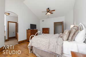 Bedroom with vaulted ceiling, light wood-style flooring, arched walkways, and a ceiling fan