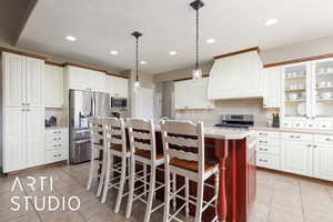 Kitchen with stainless steel appliances, custom exhaust hood, light tile patterned floors, light countertops, and a kitchen island with sink