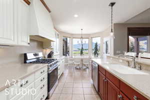 Kitchen with appliances with stainless steel finishes, custom exhaust hood, a chandelier, decorative light fixtures, and light tile patterned floors