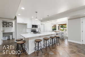 Kitchen featuring stainless steel appliances, backsplash, white cabinets, recessed lighting, and a center island with sink