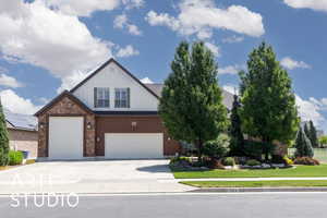 View of front of house with board and batten siding, a front lawn, driveway, brick siding, and a garage