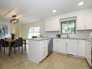 Kitchen featuring dishwasher, a peninsula, backsplash, white cabinetry, and recessed lighting