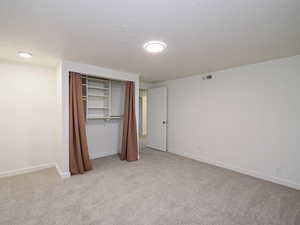 Unfurnished bedroom with light colored carpet, a textured ceiling, and a closet