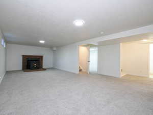 Unfurnished living room with a textured ceiling, light colored carpet, and stairway