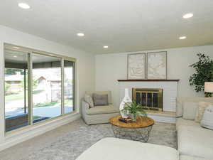 Living area with carpet flooring, recessed lighting, a textured ceiling, and a brick fireplace