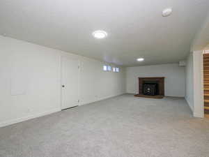 Unfurnished living room featuring stairs, light colored carpet, a brick fireplace, and a textured ceiling