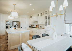 Kitchen featuring stainless steel appliances, custom range hood, light wood-style floors, recessed lighting, and a center island with sink