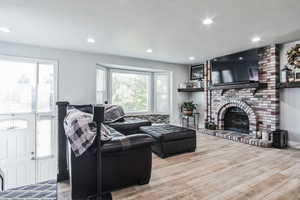 Living area with wood finished floors, a brick fireplace, recessed lighting, and a textured ceiling