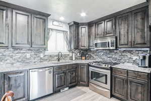 Kitchen with appliances with stainless steel finishes, tasteful backsplash, light wood finished floors, light stone counters, and a textured ceiling