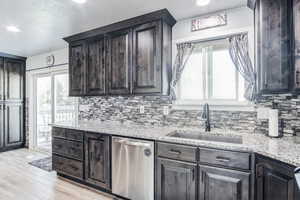 Kitchen with stainless steel dishwasher, light wood finished floors, tasteful backsplash, light stone counters, and a textured ceiling