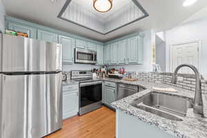 Kitchen featuring appliances with stainless steel finishes, light wood-type flooring, light stone counters, and blue cabinets