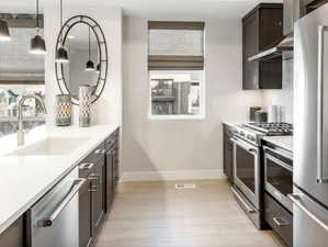 Kitchen featuring stainless steel appliances, dark brown cabinets, range hood, light countertops, and tasteful backsplash