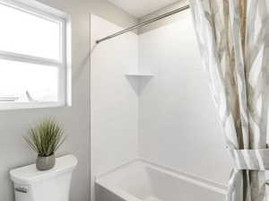 Bathroom featuring toilet and shower / bath combination with curtain