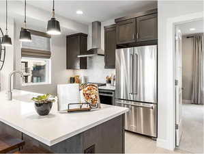 Kitchen with high end refrigerator, wall chimney range hood, dark brown cabinets, light countertops, and pendant lighting