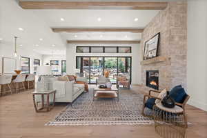 Living room featuring beam ceiling, a stone fireplace, recessed lighting, and light wood finished floors