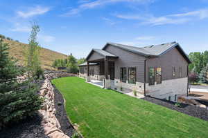 Back of property featuring stone siding, a yard, a patio, and roof with shingles