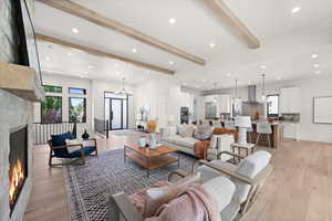 Living area featuring a lit fireplace, beam ceiling, recessed lighting, light wood-type flooring, and a chandelier
