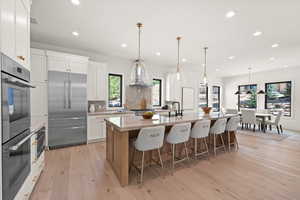 Kitchen featuring appliances with stainless steel finishes, light wood-type flooring, a kitchen bar, an island with sink, and white cabinets