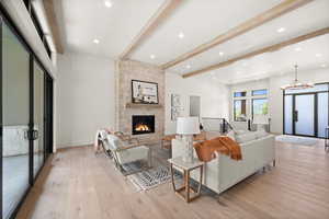 Living room featuring beamed ceiling, light wood-style flooring, a stone fireplace, a chandelier, and recessed lighting