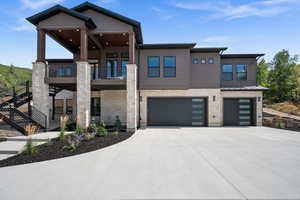Modern home featuring stone siding, a garage, driveway, and a balcony