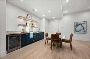 Dining space with wine cooler, bar with sink, light wood-style flooring, and recessed lighting