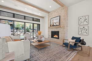 Living area featuring beam ceiling, wood finished floors, a stone fireplace, recessed lighting, and a high ceiling