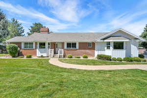 Single story home featuring brick siding, a chimney, a front lawn, and a shingled roof