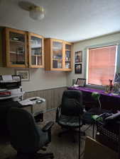 Office space with a textured ceiling, wainscoting, carpet, and wood walls