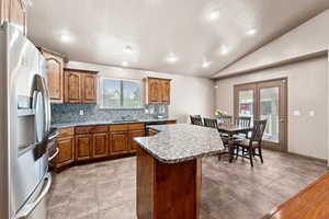 Kitchen featuring stainless steel appliances, brown cabinets, a kitchen island, backsplash, and lofted ceiling