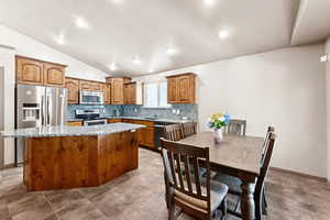 Kitchen with appliances with stainless steel finishes, vaulted ceiling, a kitchen island, brown cabinets, and tasteful backsplash