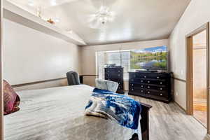 Bedroom with wood finished floors, lofted ceiling, a ceiling fan, a textured ceiling, and connected bathroom