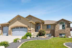 View of front of property featuring an attached garage, a front yard, driveway, stucco siding, and brick siding