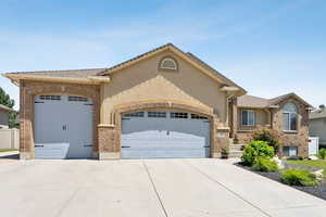 View of front of property featuring an attached garage, concrete driveway, brick siding, and stucco siding