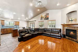 Living room with ceiling fan, a tile fireplace, light wood-style flooring, lofted ceiling, and recessed lighting