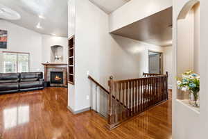 Corridor featuring an upstairs landing, wood finished floors, a textured ceiling, built in shelves, and vaulted ceiling