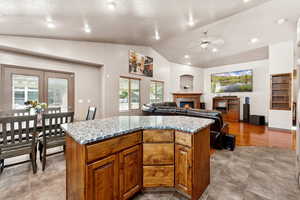 Kitchen with lofted ceiling, a glass covered fireplace, a kitchen island, light stone counters, and brown cabinets