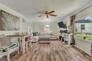 Living room featuring a textured ceiling, wood finished floors, a ceiling fan, and ornamental molding