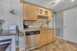 Kitchen featuring stainless steel dishwasher, light brown cabinets, backsplash, glass insert cabinets, and a textured ceiling