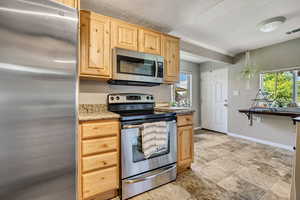 Kitchen featuring appliances with stainless steel finishes, light brown cabinetry, a textured ceiling, and light stone countertops