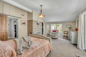 Bedroom with vaulted ceiling, a brick fireplace, a textured ceiling, and light colored carpet