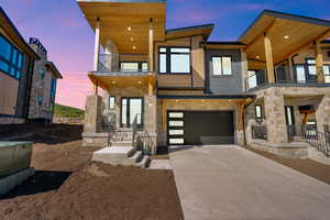Modern home with a balcony, stone siding, concrete driveway, and a garage