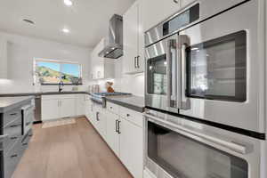 Kitchen featuring wall chimney range hood, gas stovetop, double oven, light wood-style floors, and recessed lighting