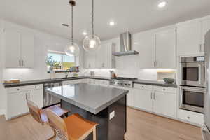 Kitchen featuring stainless steel appliances, wall chimney exhaust hood, light wood finished floors, a kitchen breakfast bar, and recessed lighting