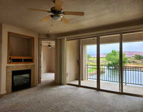 Unfurnished living room featuring a ceiling fan, carpet, a tiled fireplace, a textured ceiling, and a mountain view