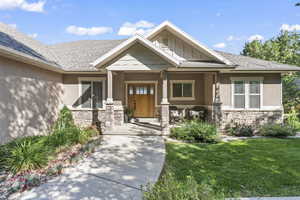 View of exterior entry featuring stucco siding, stone siding, a yard, and a shingled roof
