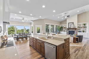 Kitchen featuring stainless steel dishwasher, ceiling fan, a center island with sink, light stone countertops, and recessed lighting