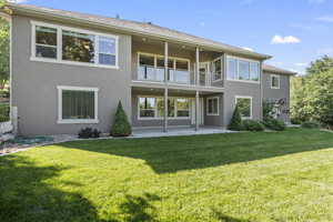 Back of property with a balcony, stucco siding, a patio area, and a yard