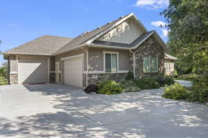 View of front of property with stone siding, an attached garage, driveway, and stucco siding