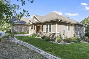 View of front of home featuring stucco siding, stone siding, a front yard, and a shingled roof